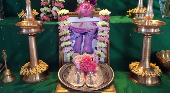 Amma's padukas on altar with lit lamps and fresh flowers