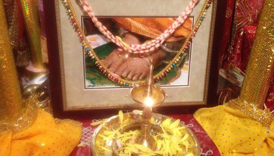 Lit brass lamp in front of photo of Amma's feet