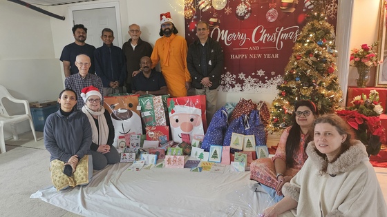 Ramanandamrita Chaitanya with Amma Canada volunteers beside Christmas tree surrounded by gifts and cards for the needy