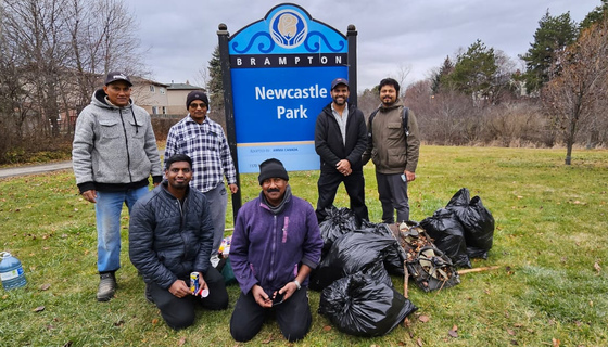 Volunteers standing near Newcastle Park sign with bags of garbage they have collected