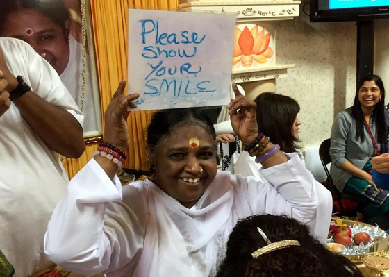 Amma smiling and holding a sign saying 'Please show your smile'
