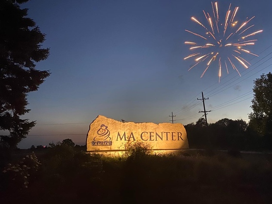 The MA Center Chicago entrance sign lit at night, with fireworks in the background