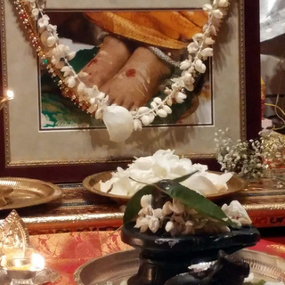 Black stone Shiva lingam and Nandi in front of garlanded photo of Amma's feet