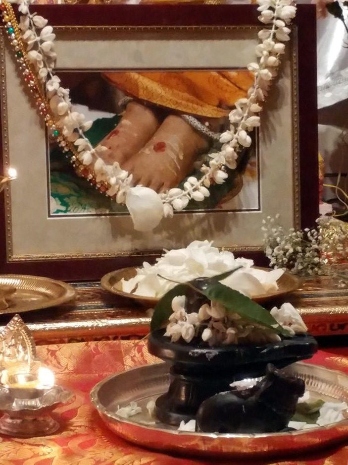 Black stone Shiva Lingam and Nandi in front of garlanded photo of Amma's feet