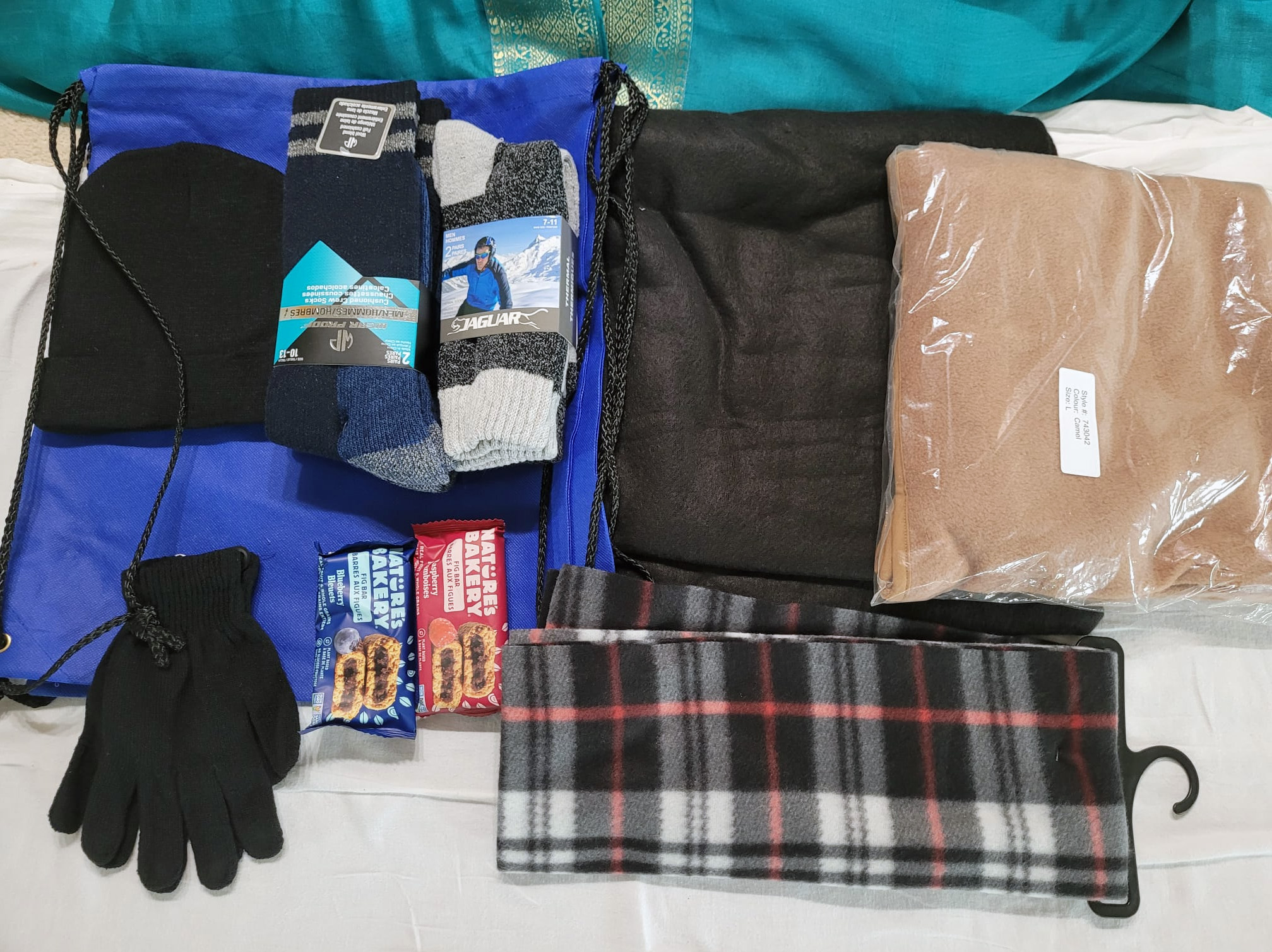 Assembled items for homeless care package: fig bag, gloves, toque, scarf, warm sock, tshirt, cinch bag