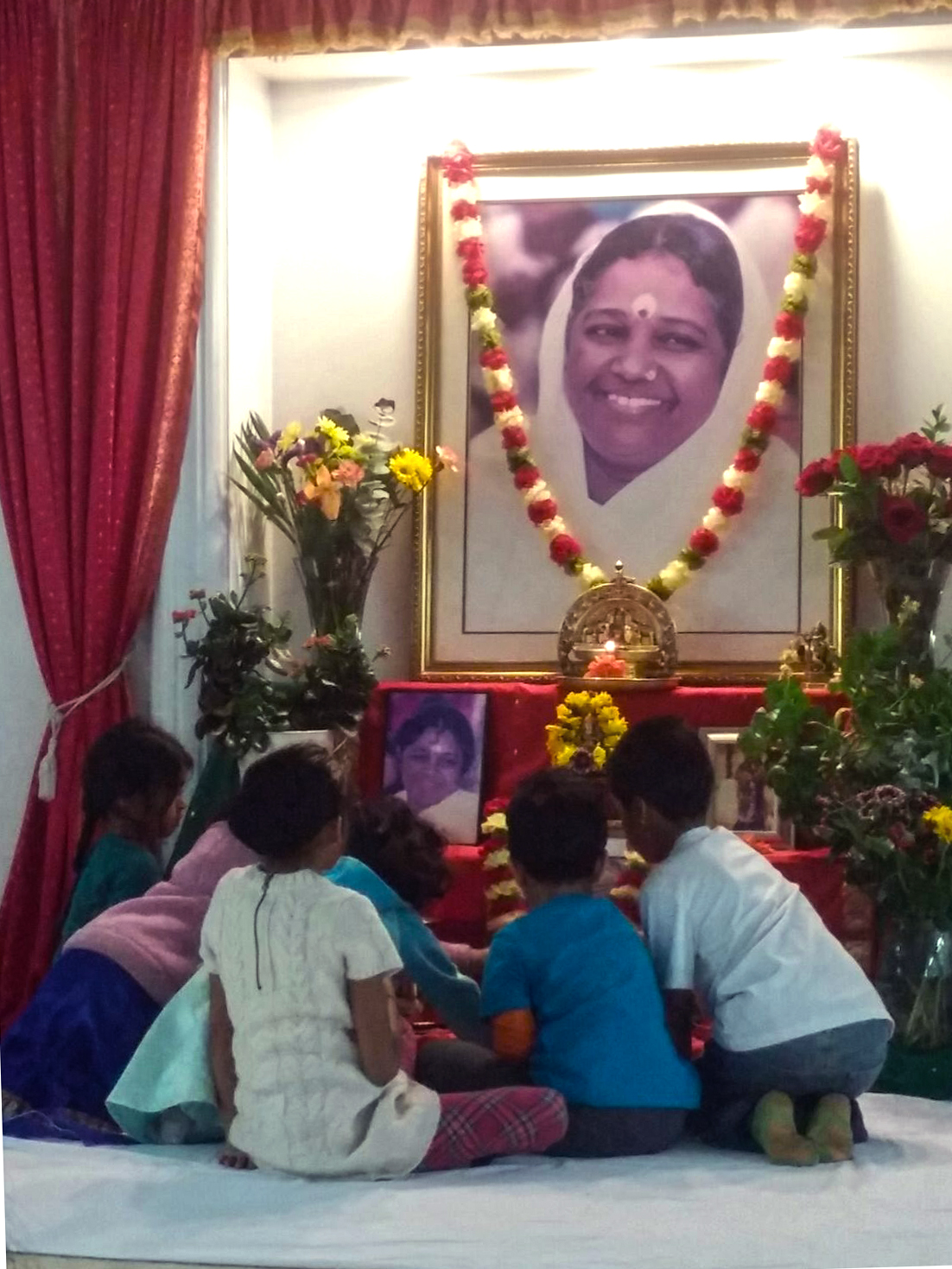 Children offering flower petals before Amma's photo on altar