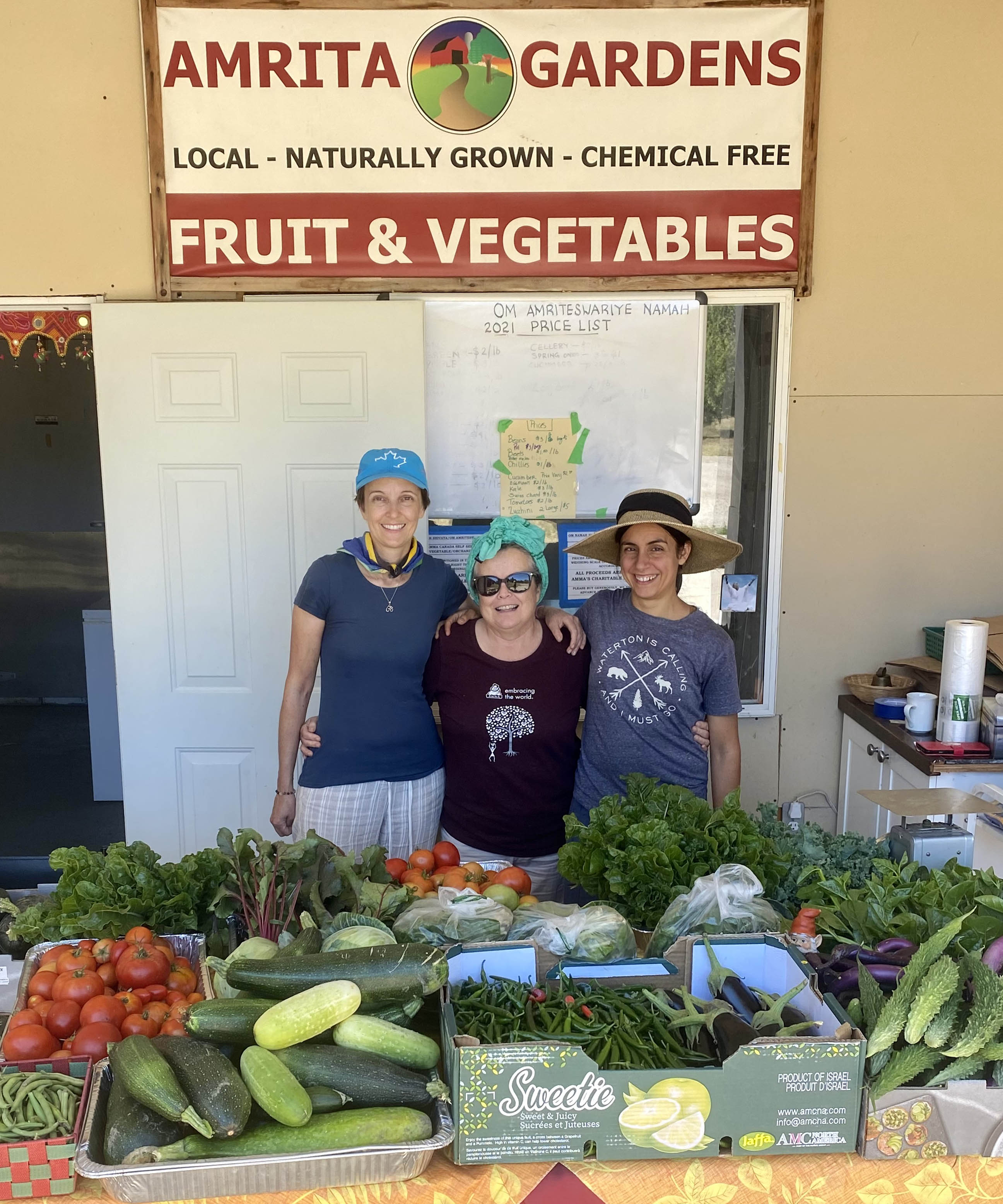 Three volunteers at the Farm stand, loaded with fresh veggies